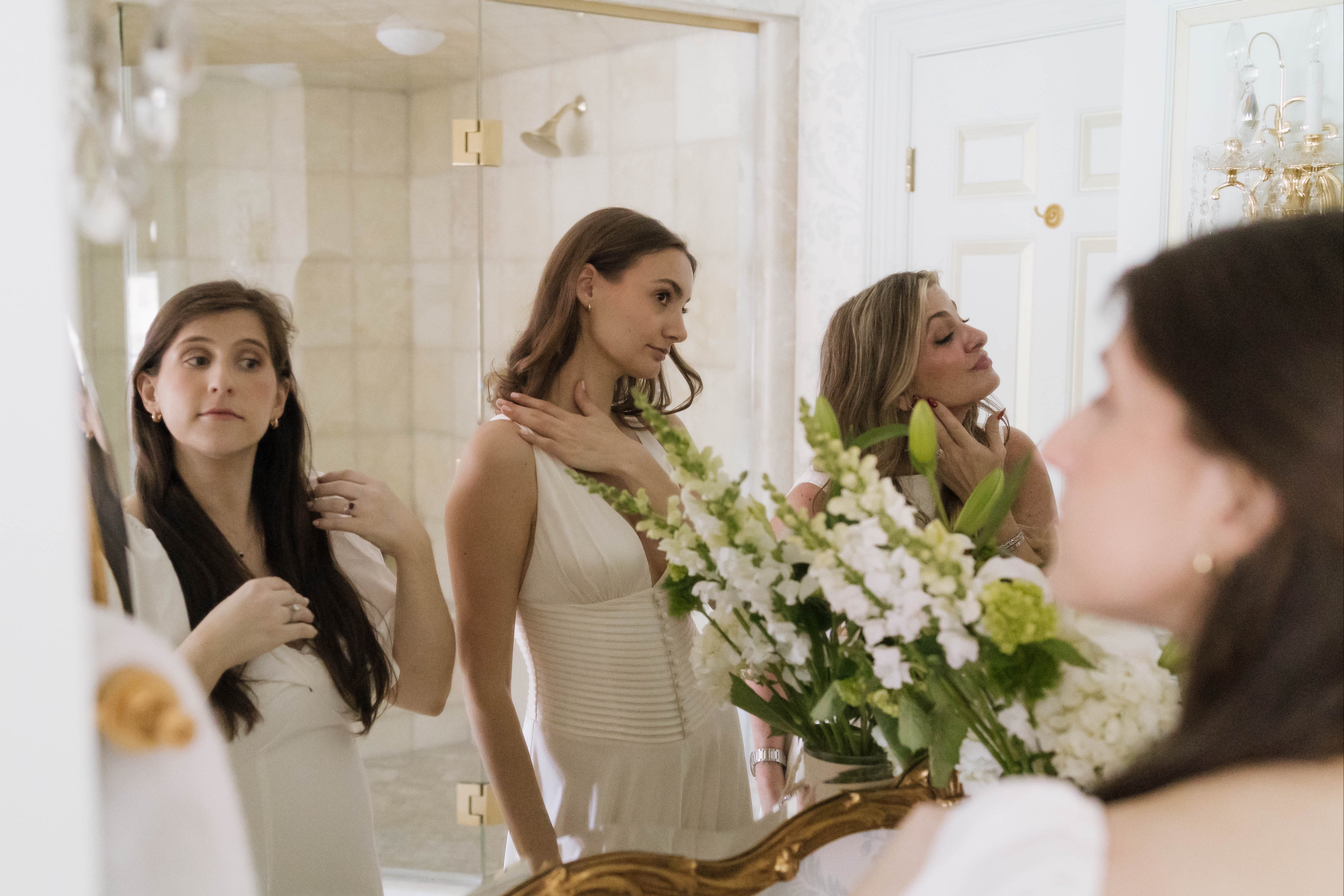Woman in a white dress standing in front of a mirror with floral decorations.
