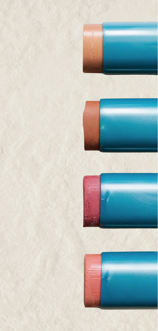 Four pastel crayons with blue bodies and pinkish-brown tips arranged vertically on the right side of a textured beige background.